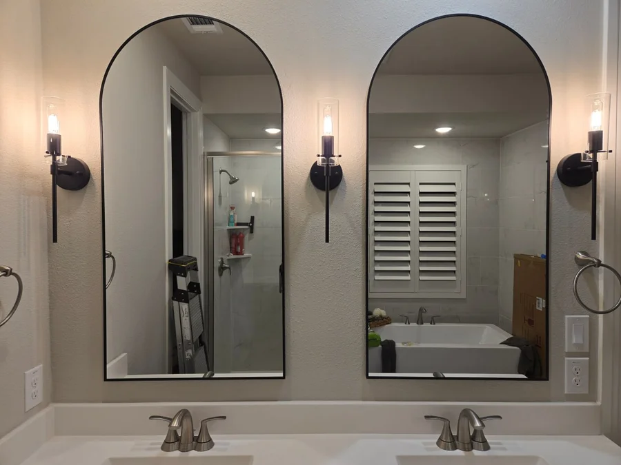 Completed bathroom renovation with double vanity, arched mirrors, and wall sconces