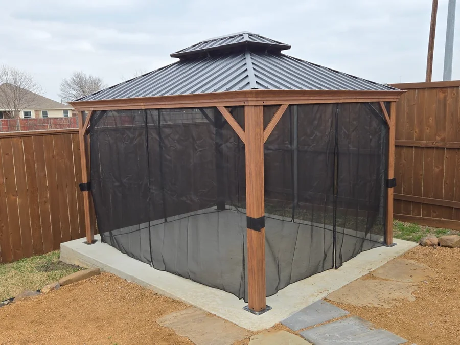 Hardtop gazebo with mesh screens installed on concrete pad in residential backyard