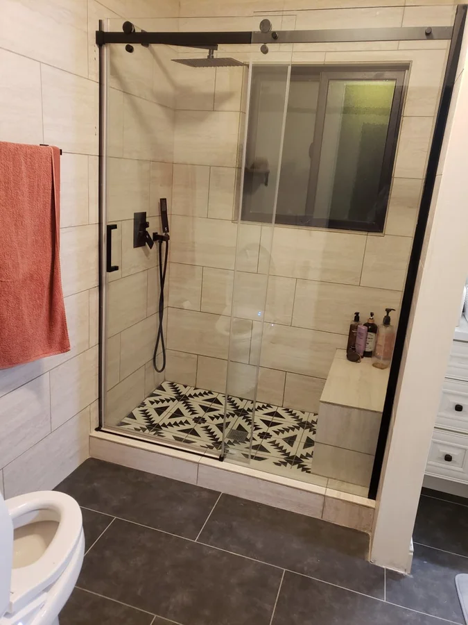 Completed walk-in shower remodel with black-framed glass enclosure and patterned mosaic tile floor